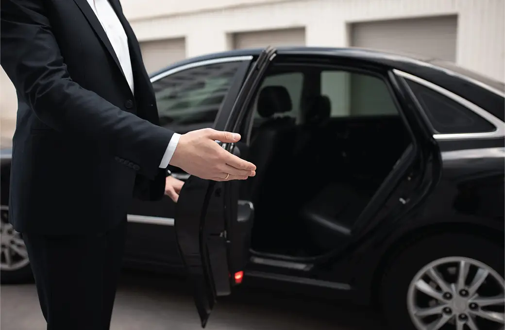 A person in a-suit is holding the door open to a black car. limo service in New York.