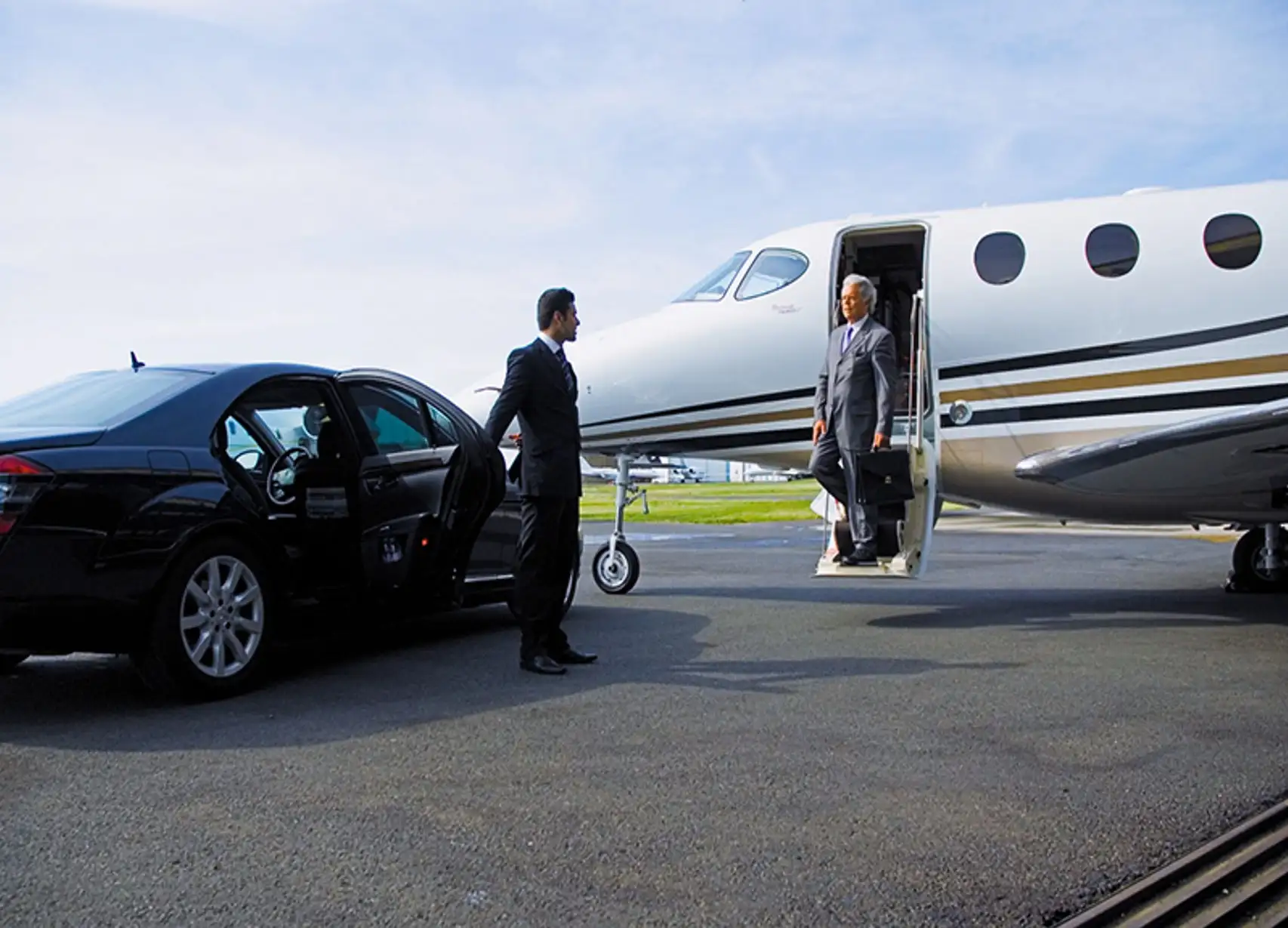 car service laguardia airport Businessman-exiting-a-private-jet-onto-the-tarmac-where-a-chauffeur-holds-open-the-door-of-a-luxury-car.